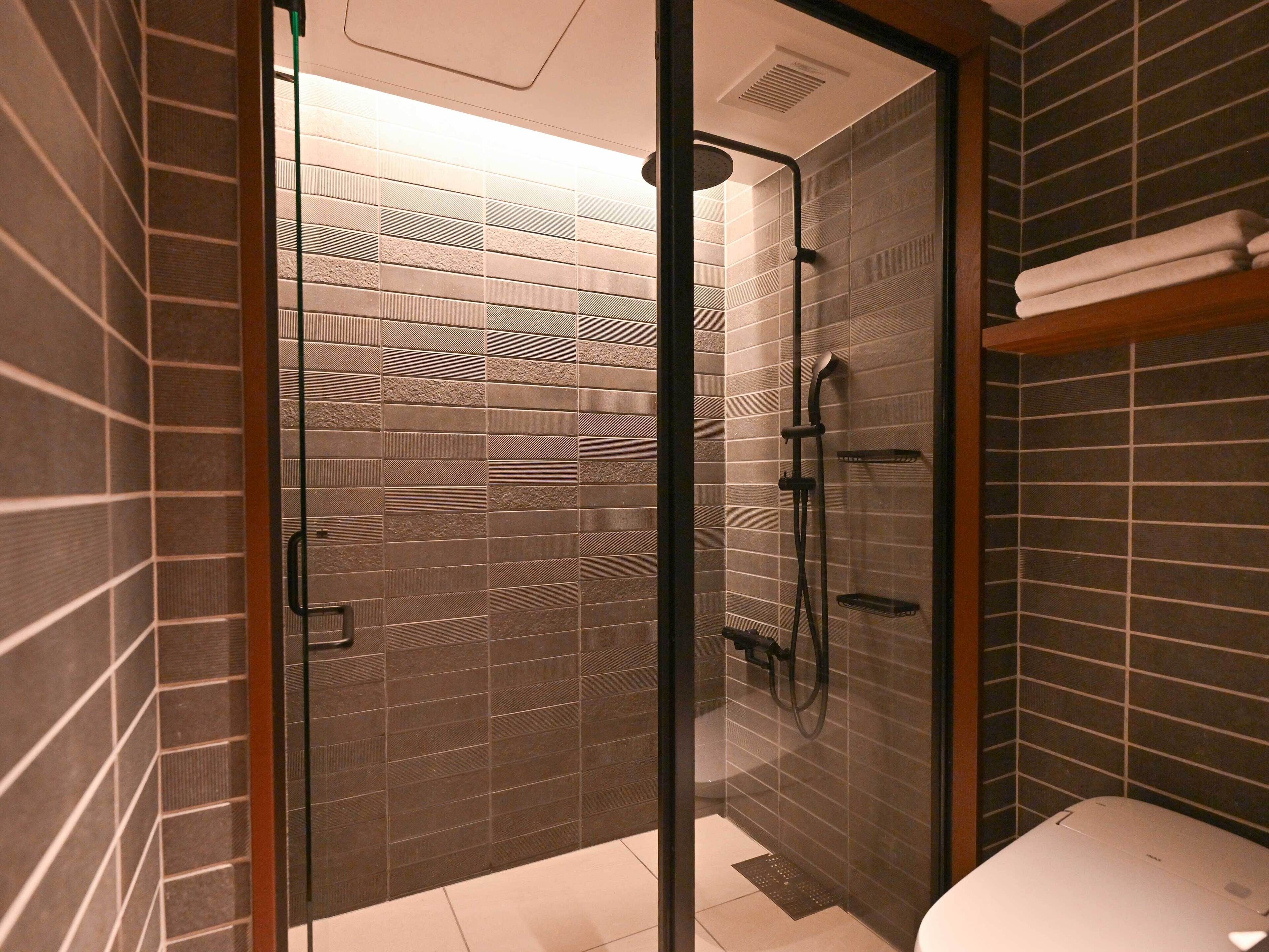 A modern bathroom with a glass-enclosed shower, tiled walls, and a toilet.