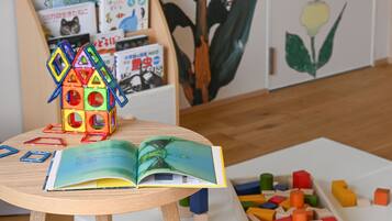 A wooden table with a colorful house-shaped toy, an open book, and a box of colorful building blocks.