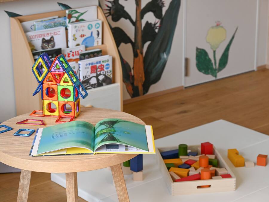 A wooden table with a colorful house-shaped toy, an open book, and a box of colorful building blocks.