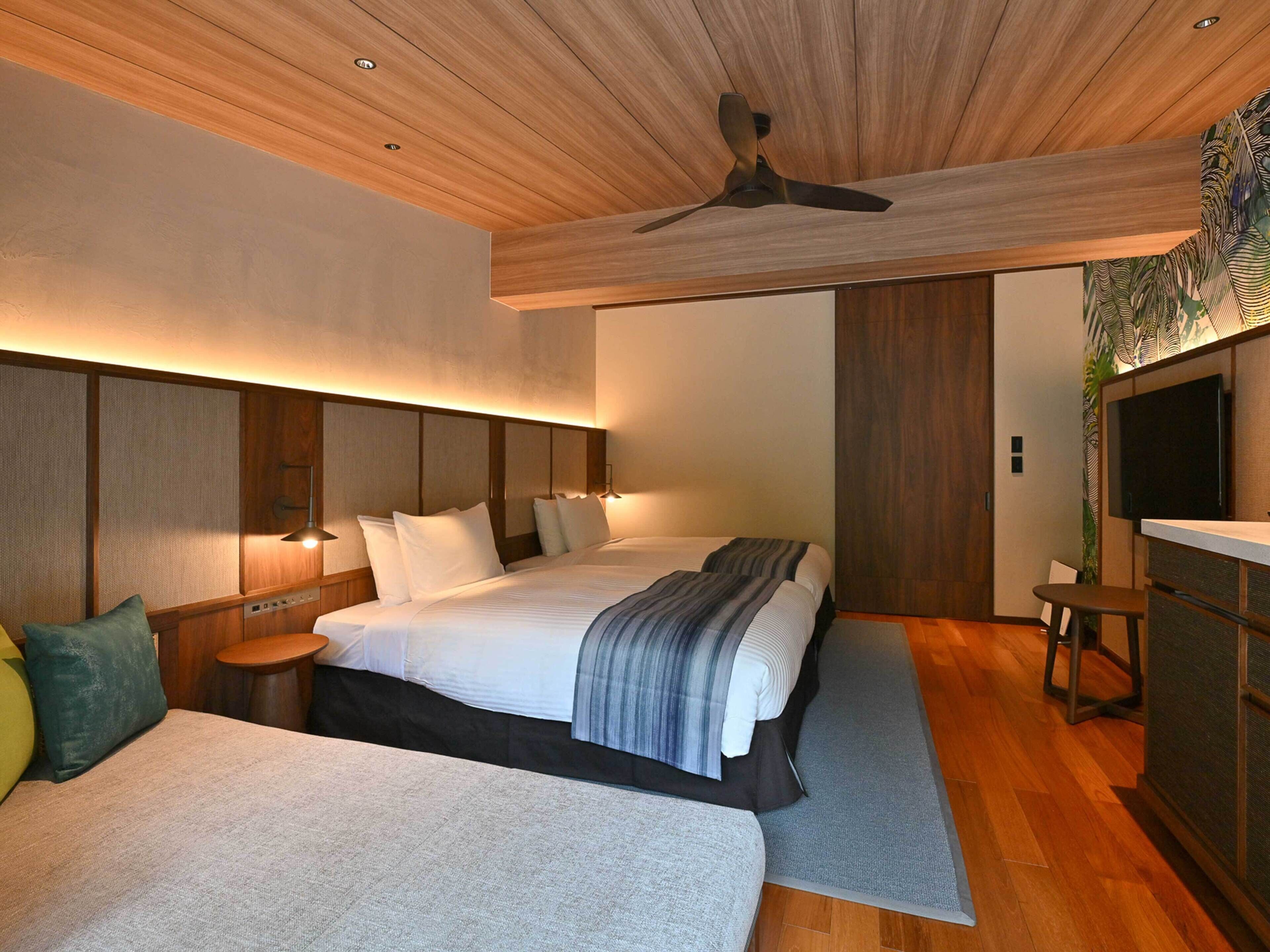 A modern hotel room with a large bed, bedside tables, a desk, and a ceiling fan.