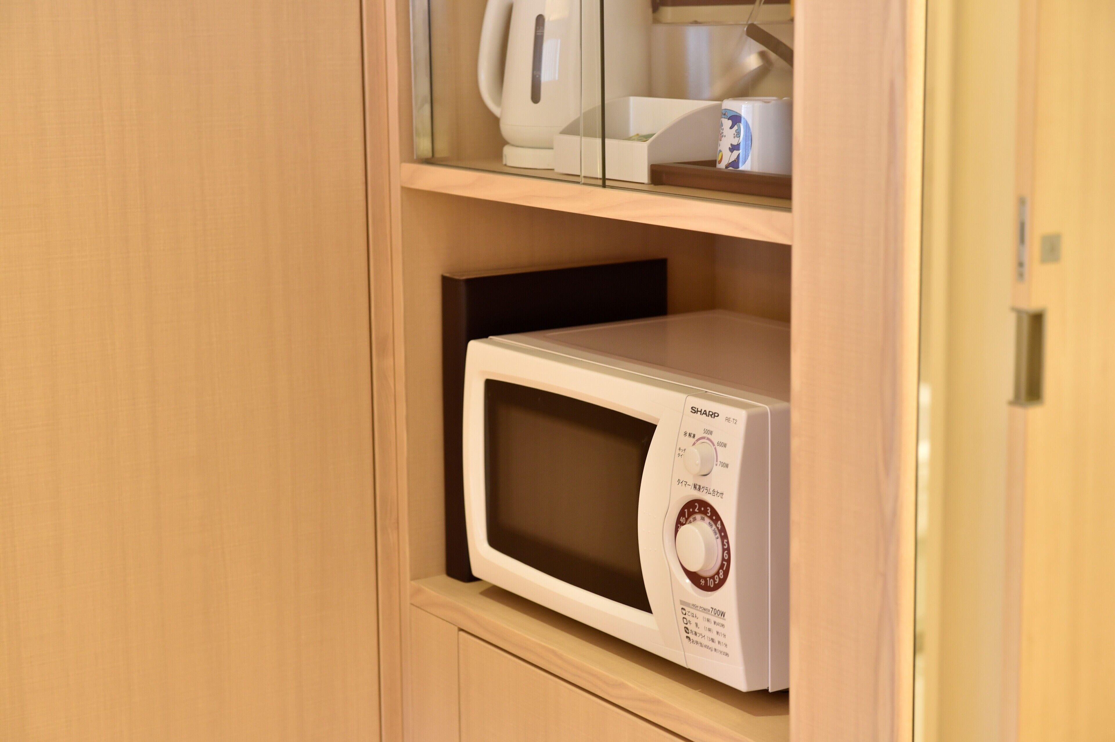 A microwave on a shelf in a kitchen area with a cabinet above it.