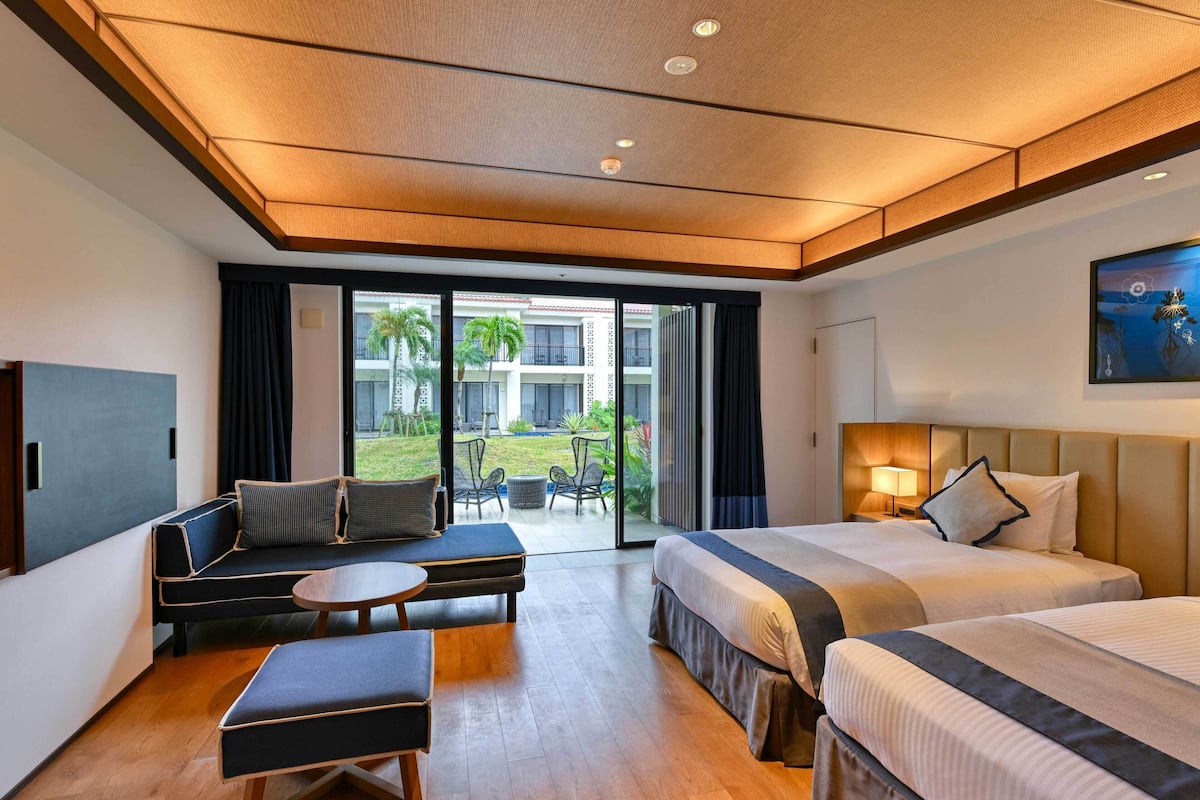 A hotel room with a bed, a sofa, a small table, and a view of the outdoor area.