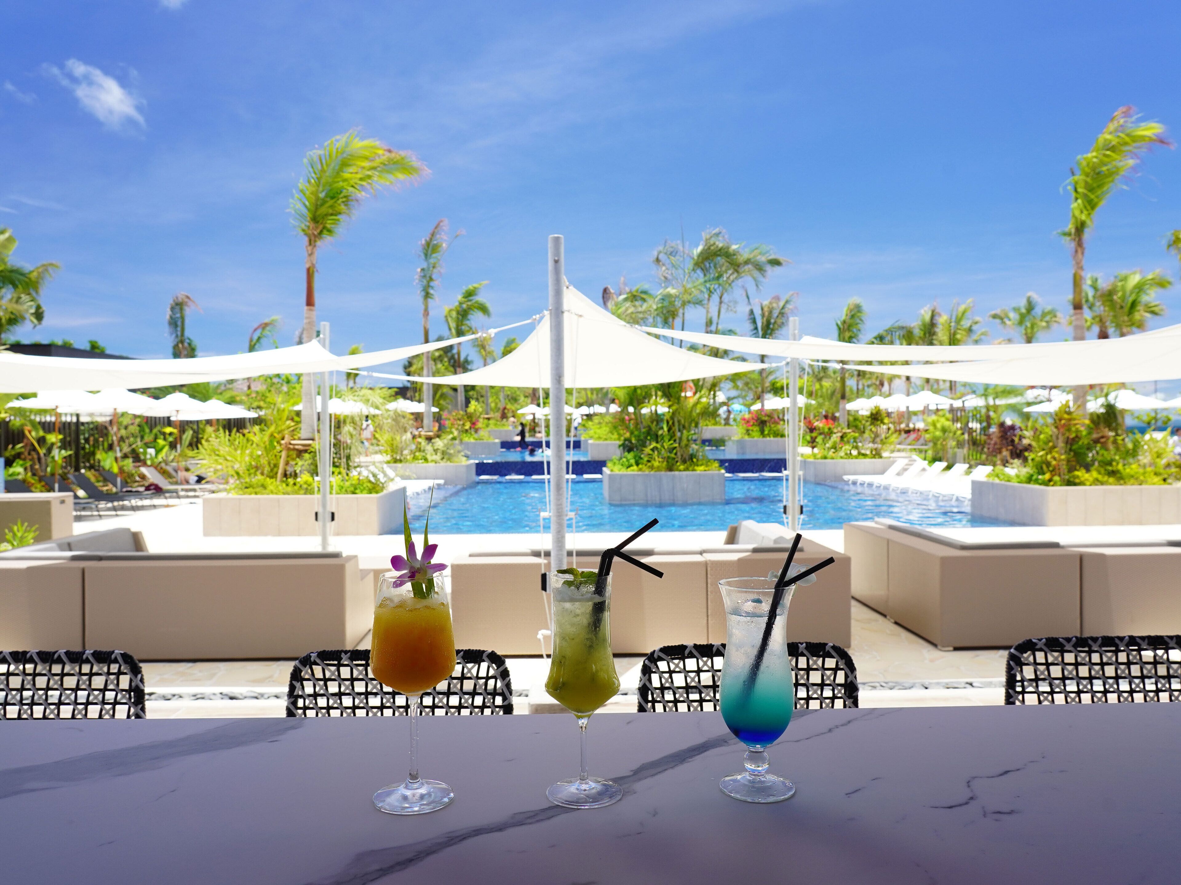 Een poolbar met drie drankjes en uitzicht op een zwembad en palmbomen.
