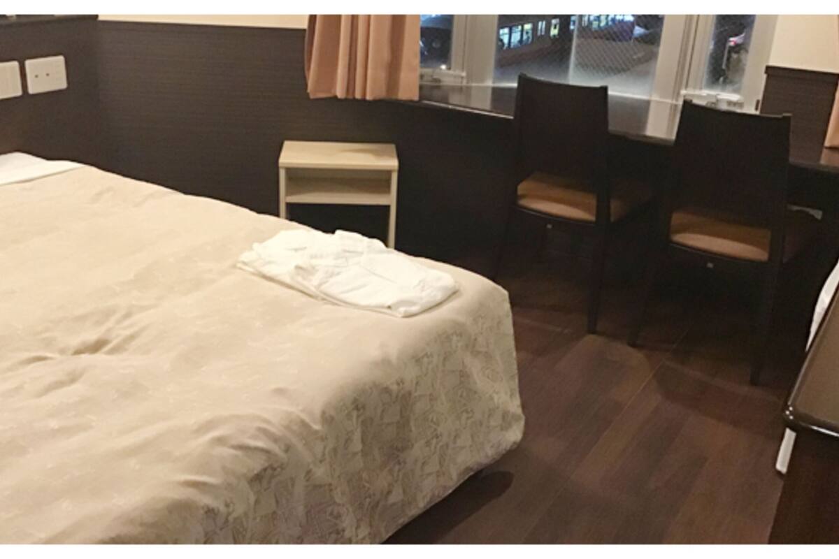 A hotel room with a large bed, a small desk, two chairs, and a window with curtains.