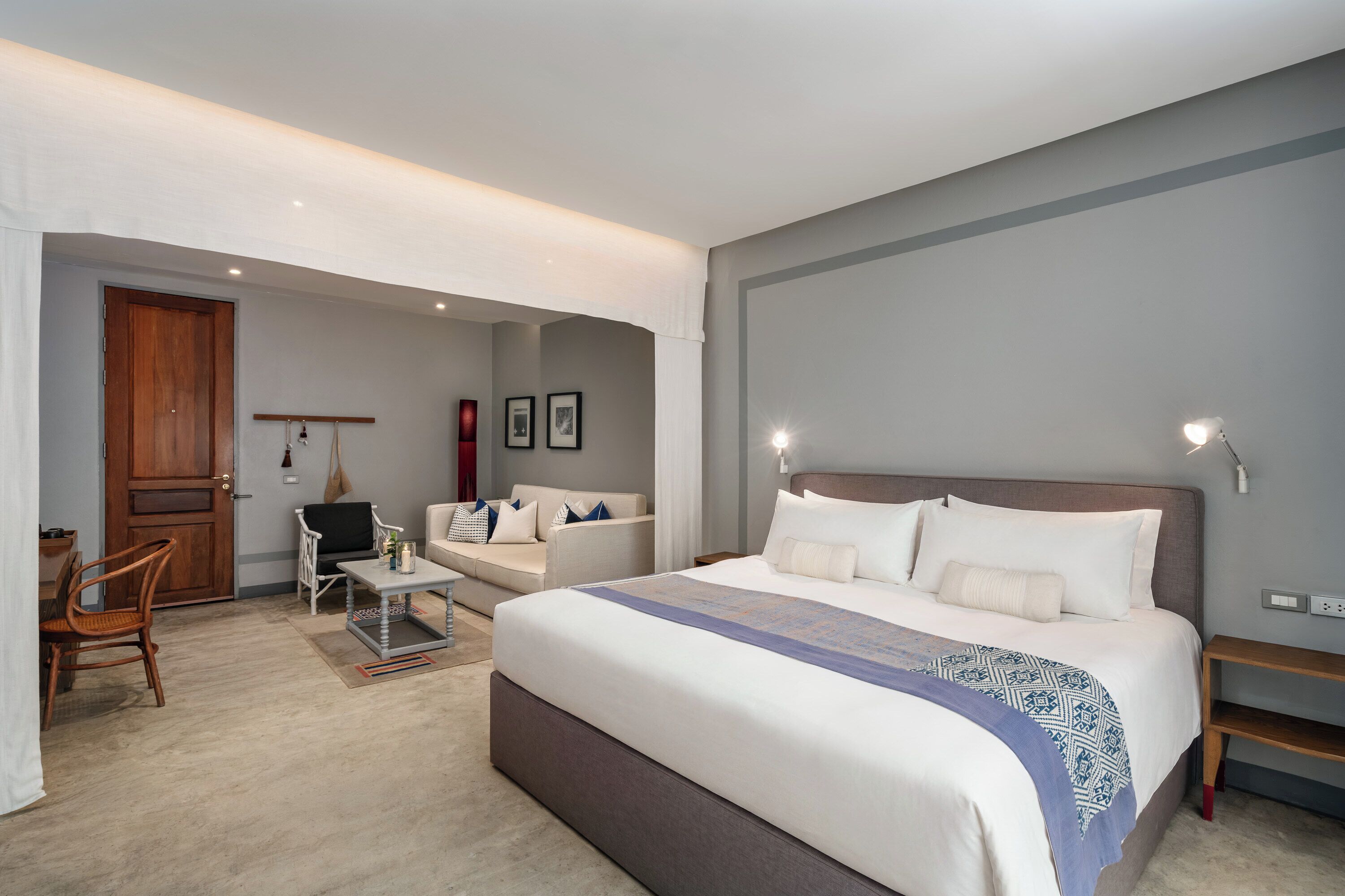 Une chambre d’hôtel avec un lit, un canapé, une chaise, une petite table et une porte.