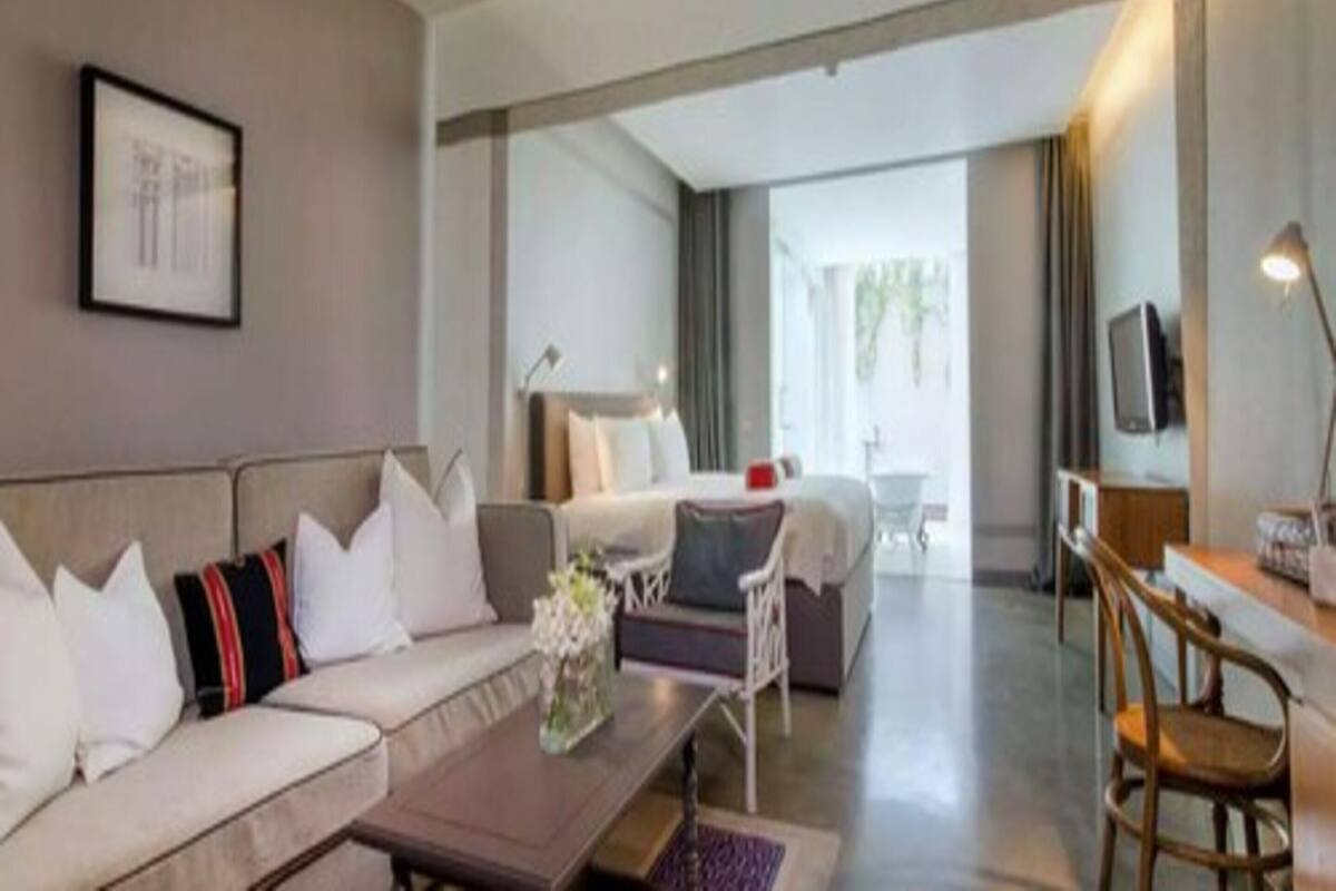 A modern hotel room with a sofa, a coffee table, a TV, and a dining area.