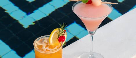 Two drinks, one in a short glass and one in a martini glass, with garnishes and a pool in the background.