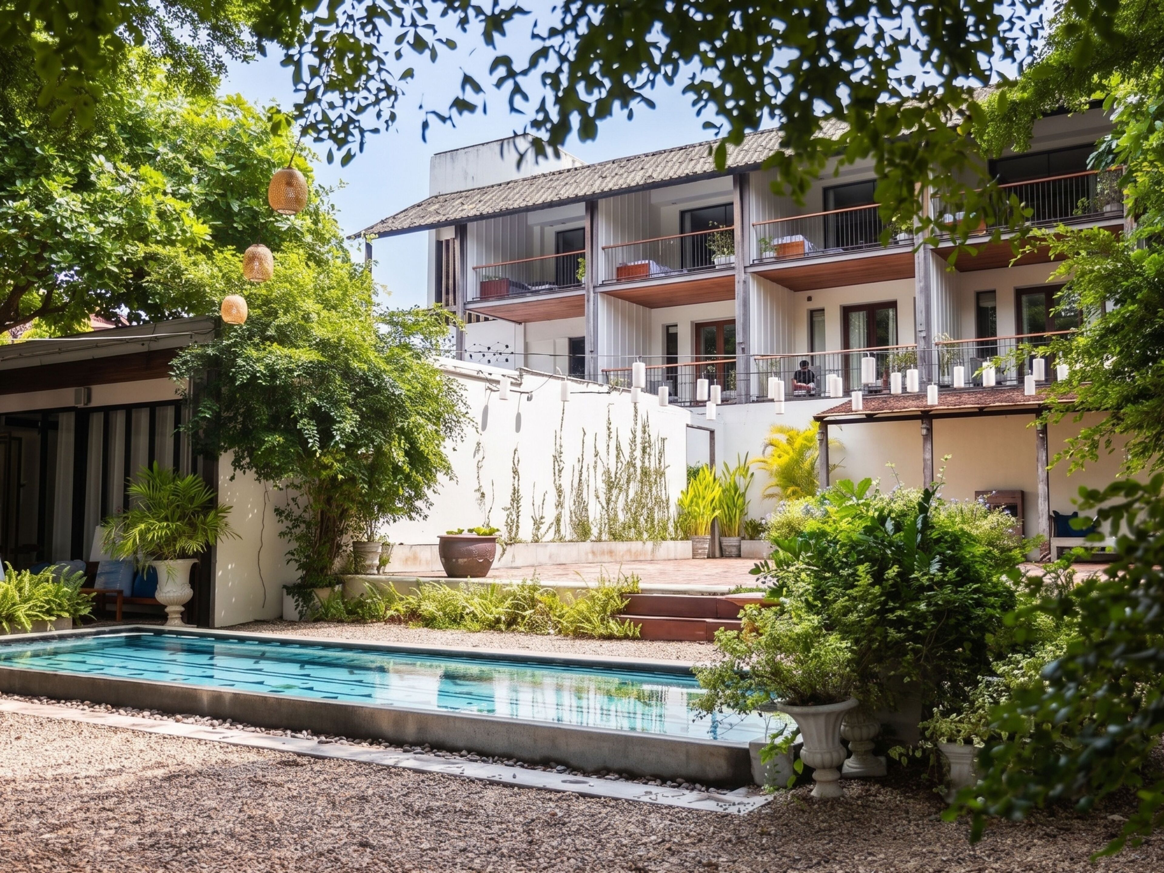 A pool area with a clear view of a building with multiple balconies and a covered outdoor seating area.