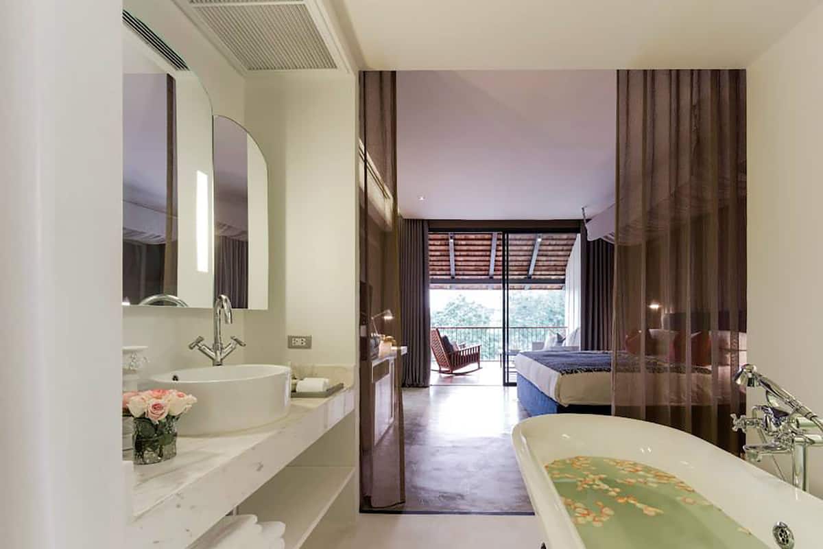 A modern bathroom with a large bathtub, a sink, and a mirror. There is a balcony with a view of the outdoors.