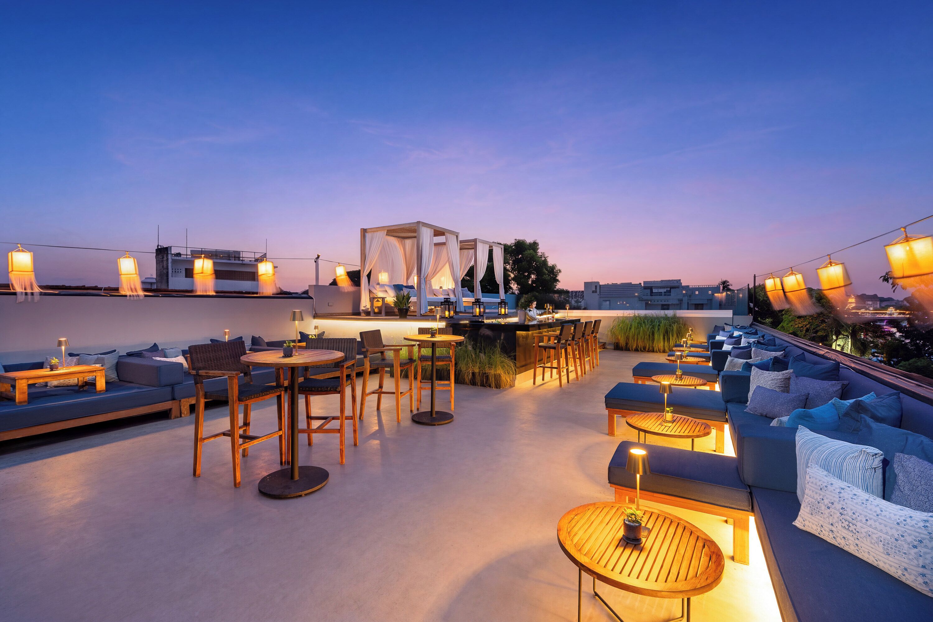 Un bar situé sur le toit, avec une terrasse, un espace bar et une vue sur les toits de la ville au crépuscule.