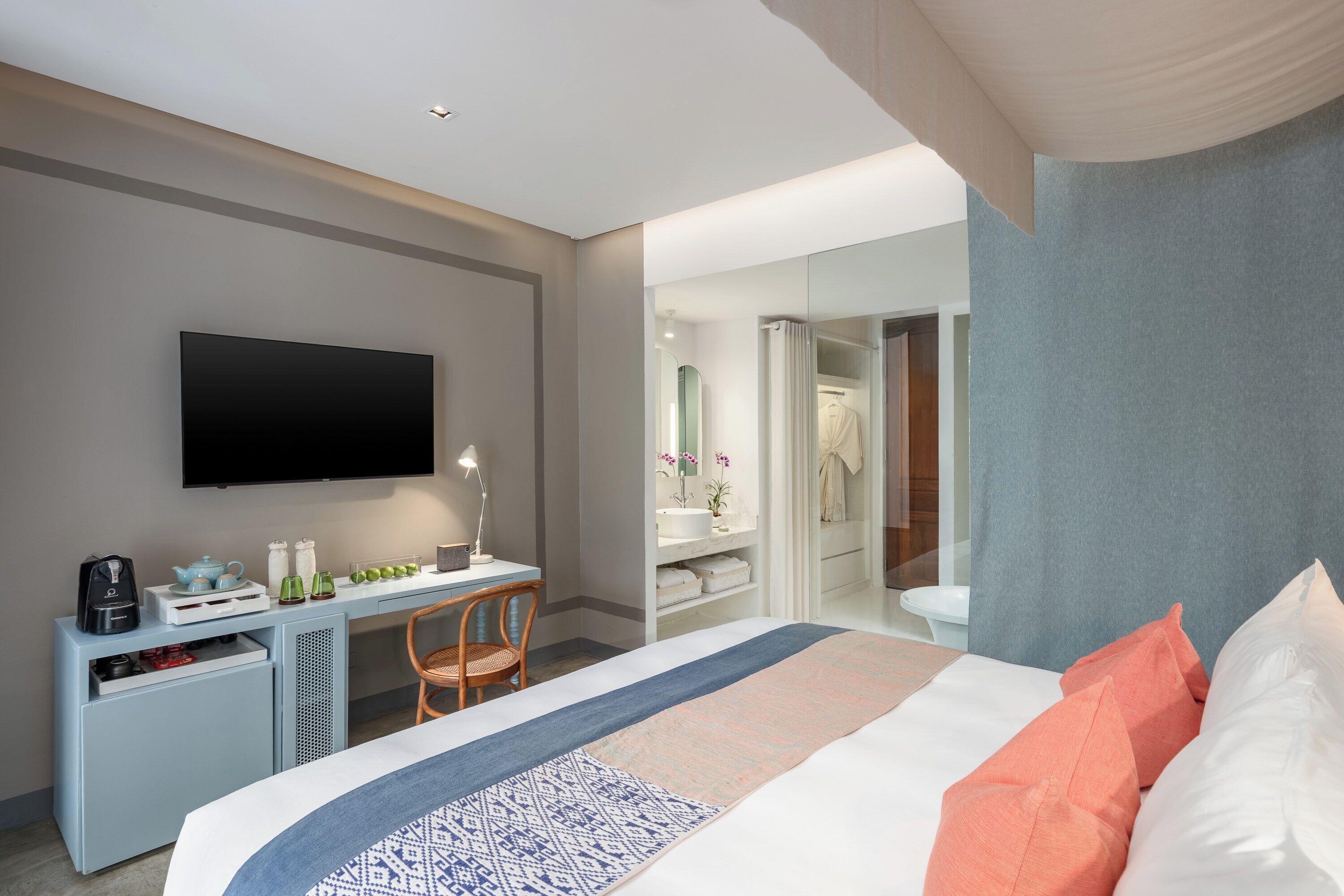 Une chambre d’hôtel moderne équipée d’un lit, d’un bureau, d’un téléviseur à écran plat et d’une salle de bain visible à travers une paroi en verre.