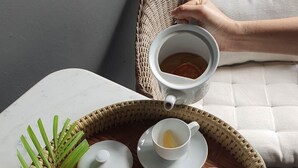 Ein Korbtablett mit einer Schale Trockenfrüchten, einer Teetasse und einem Teekessel auf einem Tisch.
