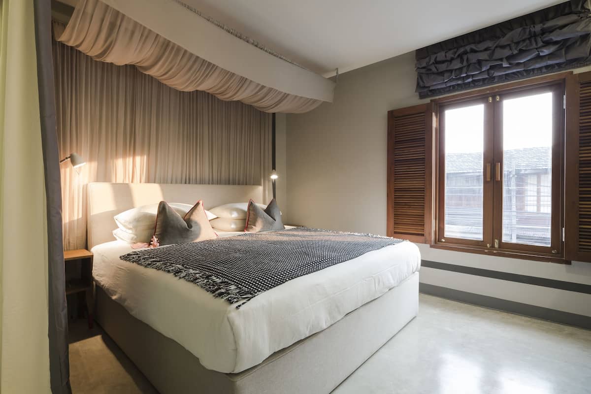 A bedroom with a large bed, a nightstand, a lamp, and a window with shutters.