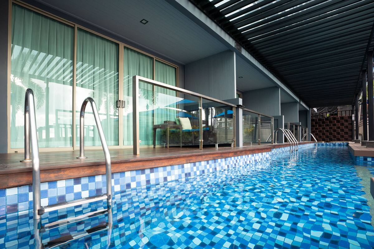 An indoor swimming pool with a tiled floor, glass railings, and a wooden deck.