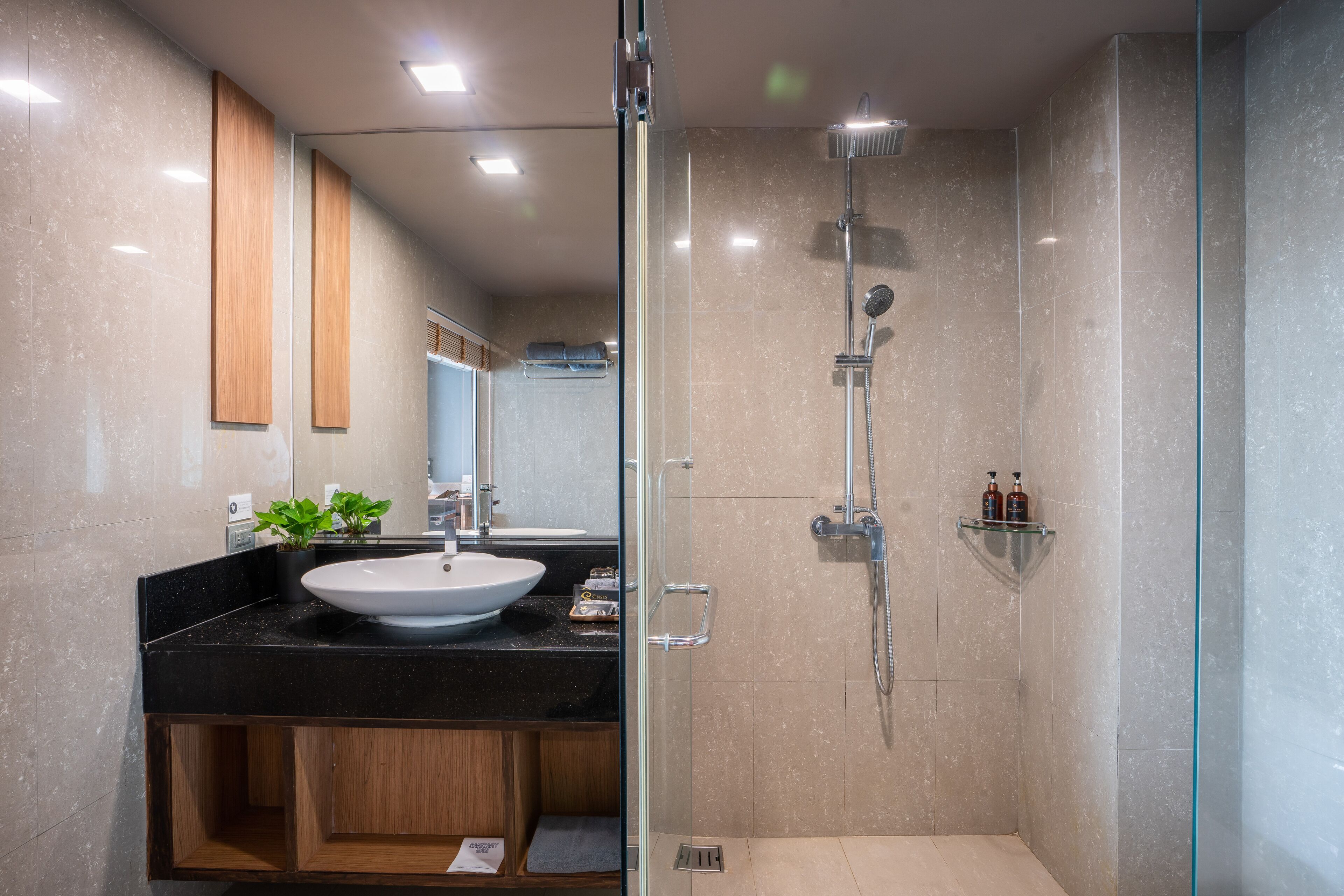Un baño moderno con ducha de vidrio, lavamanos sobre encimera negra y muebles de madera.