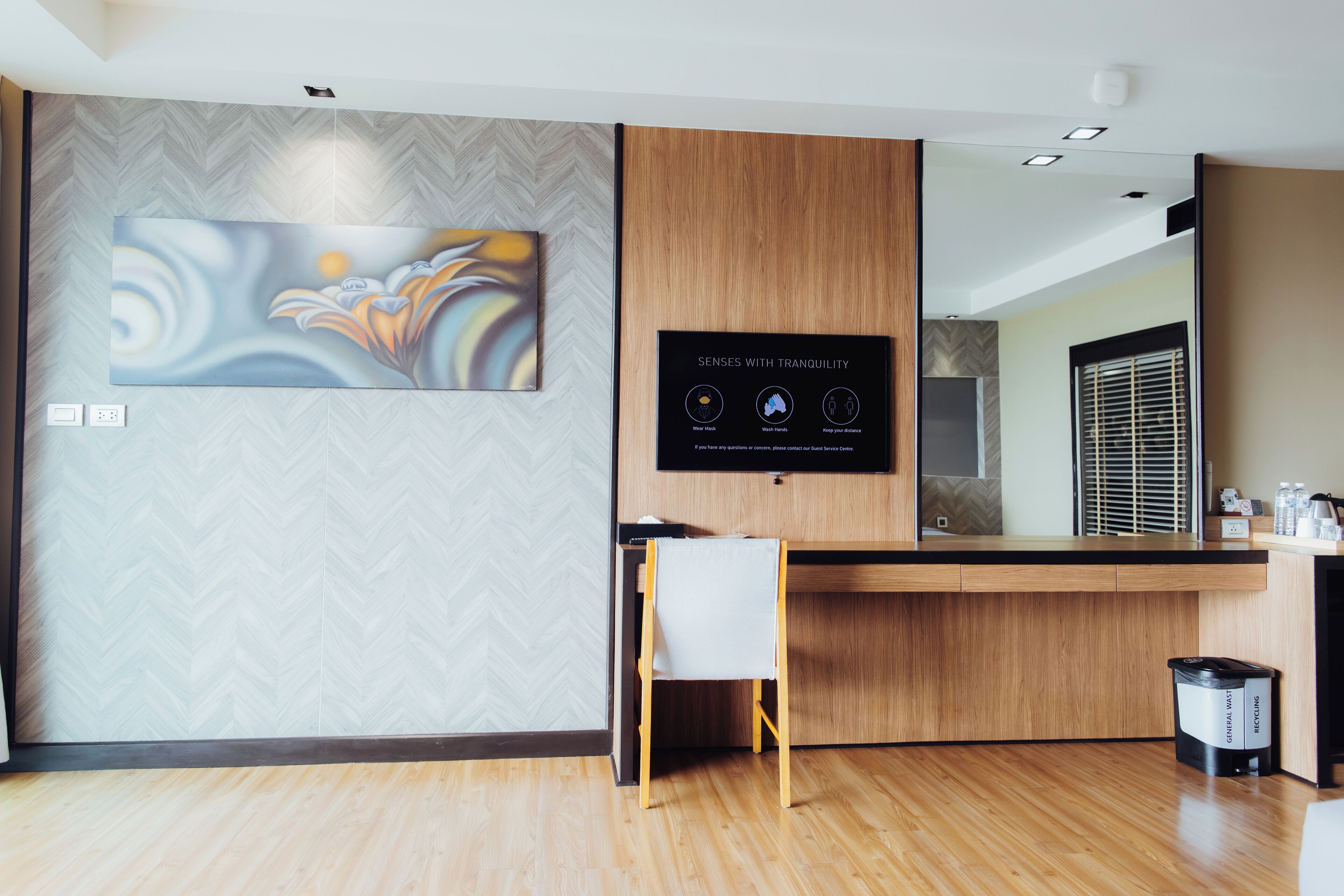 Un área de recepción moderna con una pared con diseño de espiga, un cuadro abstracto de gran tamaño, un mostrador de recepción de madera, una pequeña silla blanca y un contenedor de reciclaje.