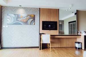 Un área de recepción moderna con una pared con diseño de espiga, un cuadro abstracto de gran tamaño, un mostrador de recepción de madera, una pequeña silla blanca y un contenedor de reciclaje.