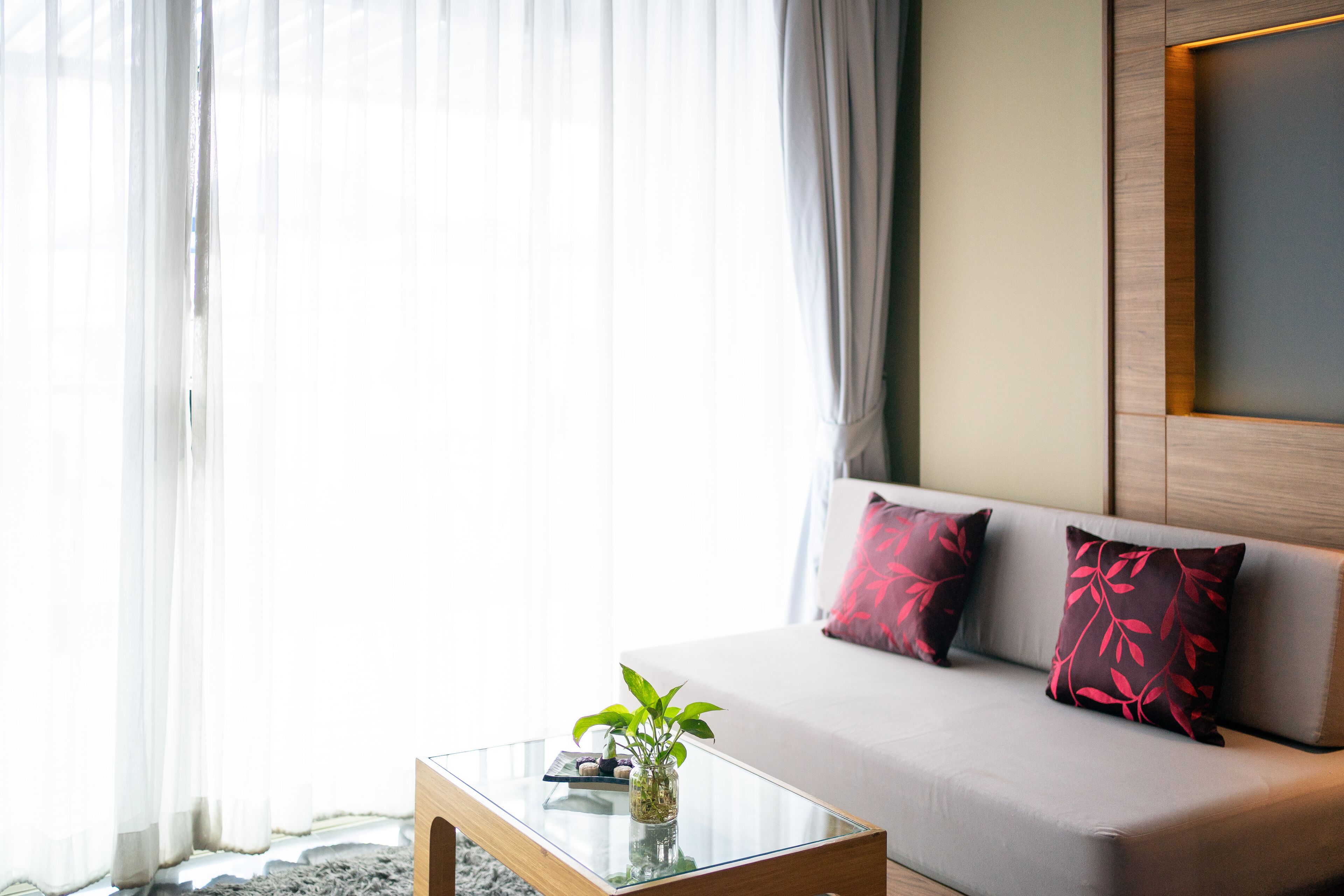 Un moderno salón con una mesa de centro de vidrio, un sofá con cojines de estampado rojo y un florero con plantas verdes.