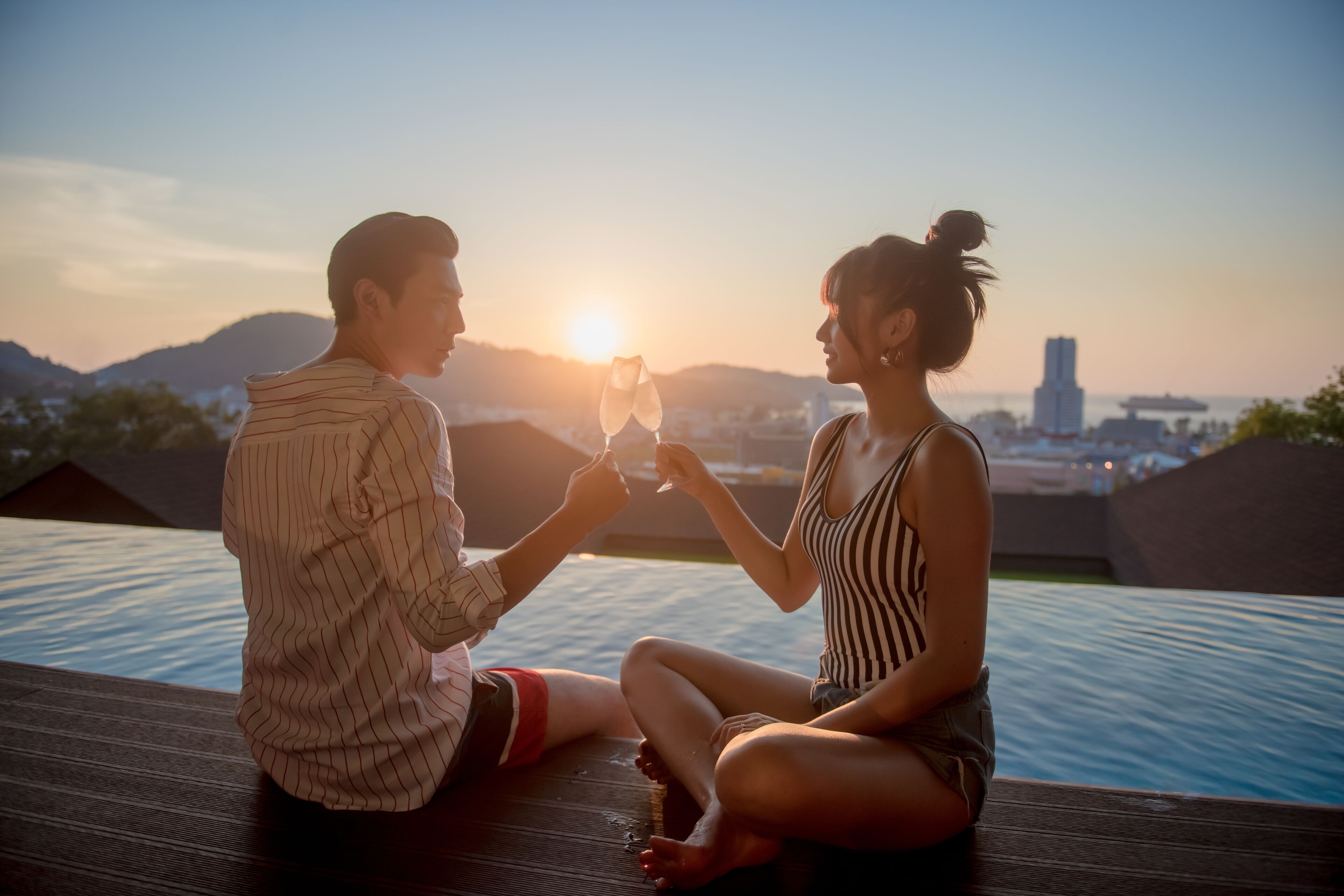 Dos personas sentadas junto a una piscina, con el atardecer de fondo.