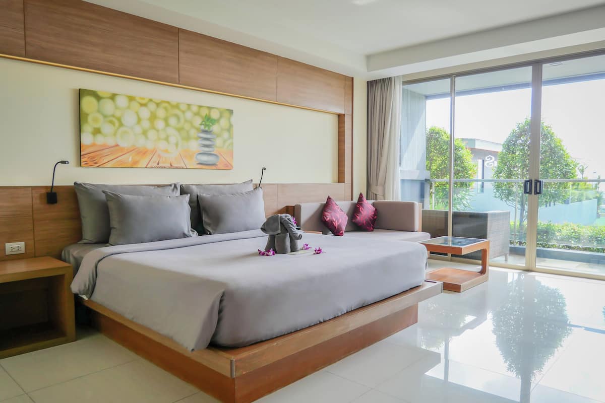 A modern hotel room with a large bed, a sofa, and a balcony with a view.