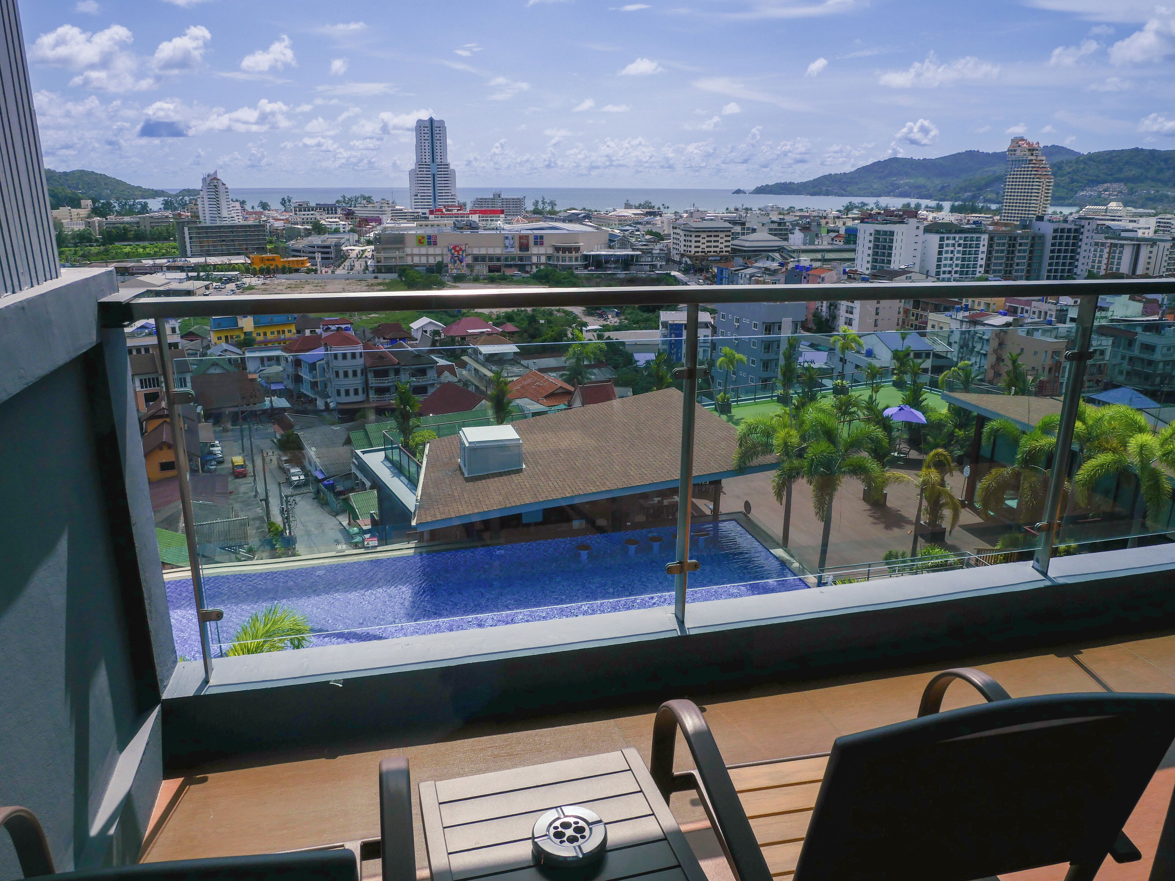 A balcony with a view of a swimming pool, cityscape, and mountains.