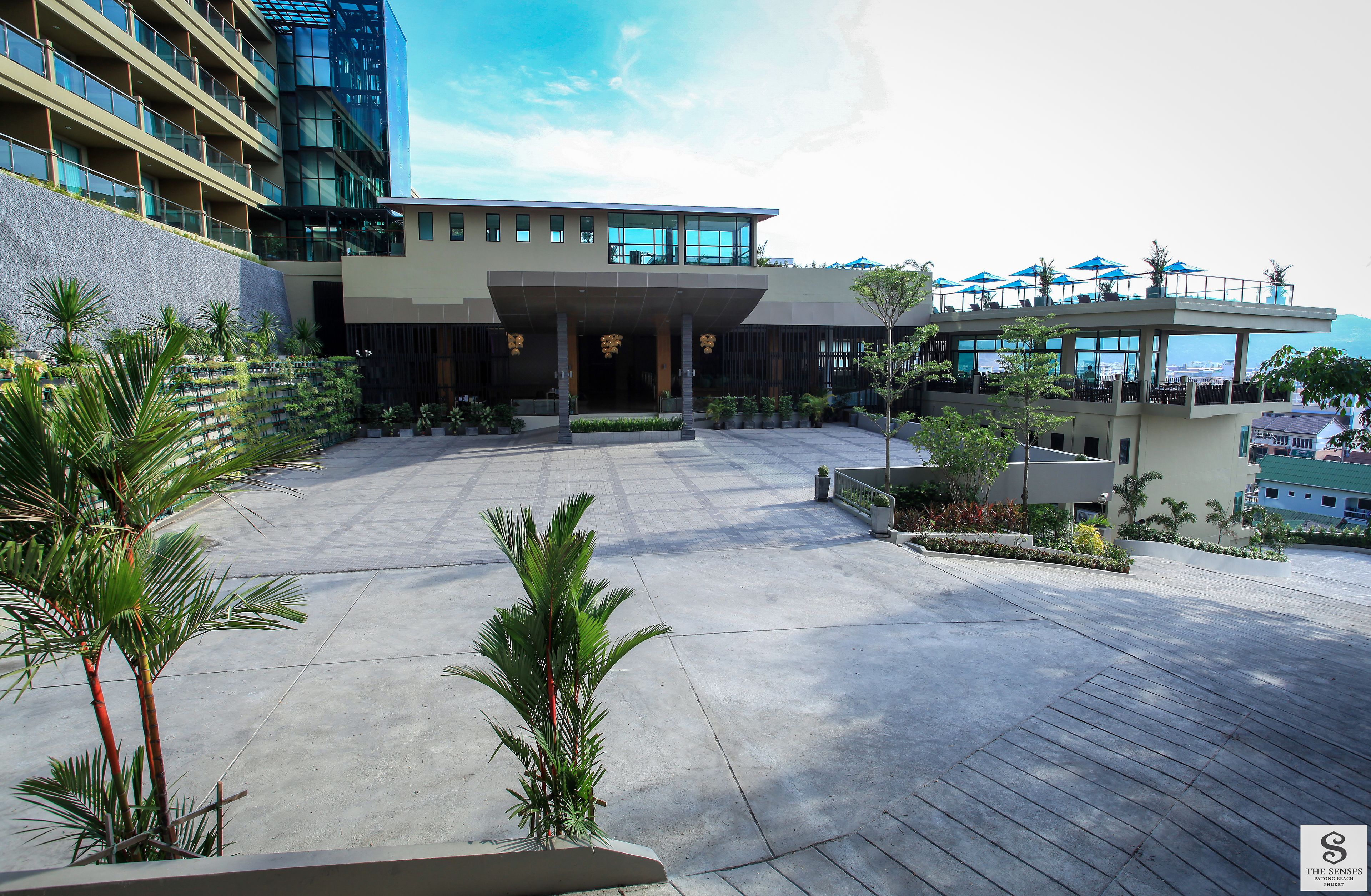 A modern hotel with a spacious courtyard, a covered entrance, and a rooftop bar with umbrellas.