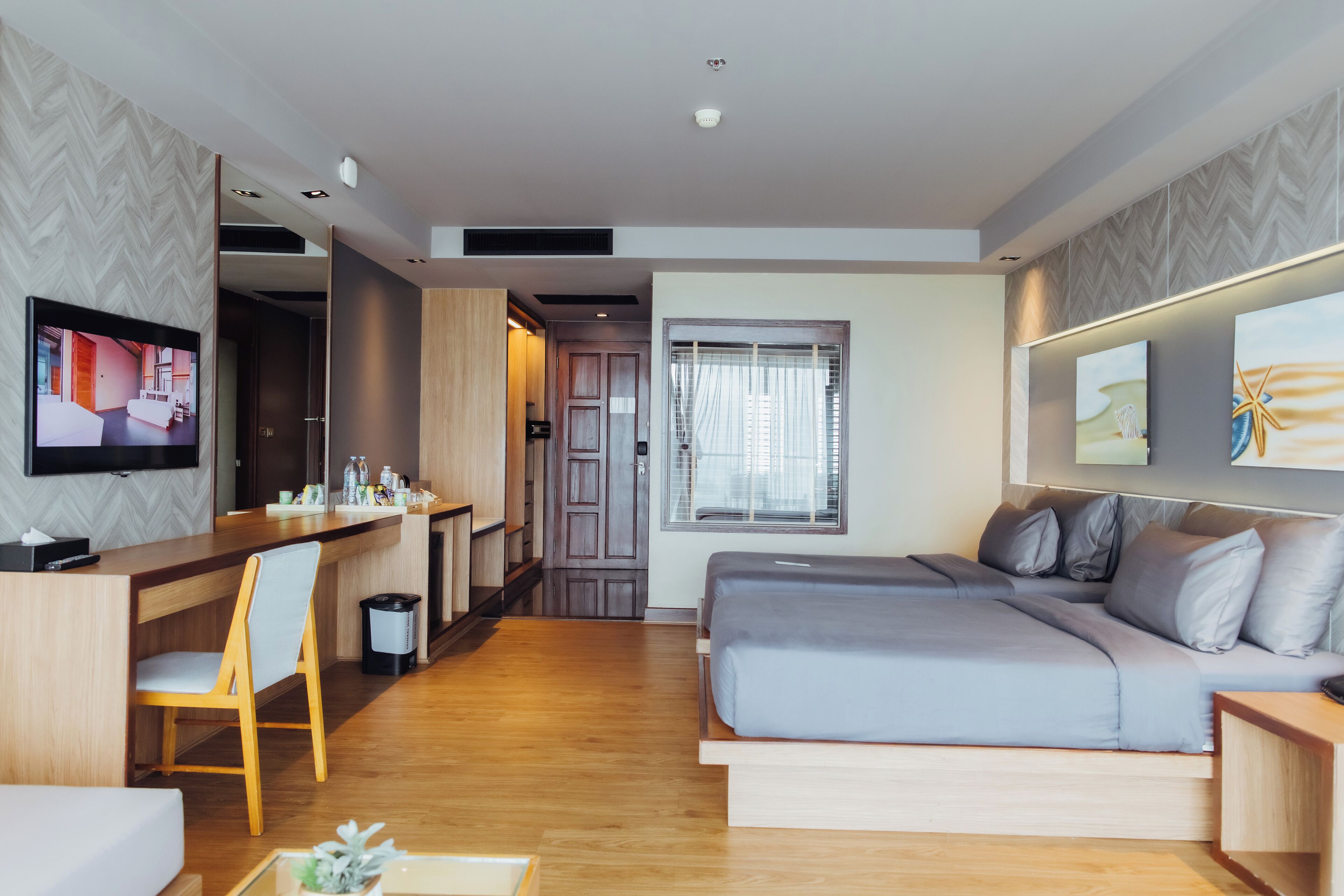 A modern hotel room with a wooden floor, a sofa bed, a desk with a chair, a TV, and artwork on the walls.