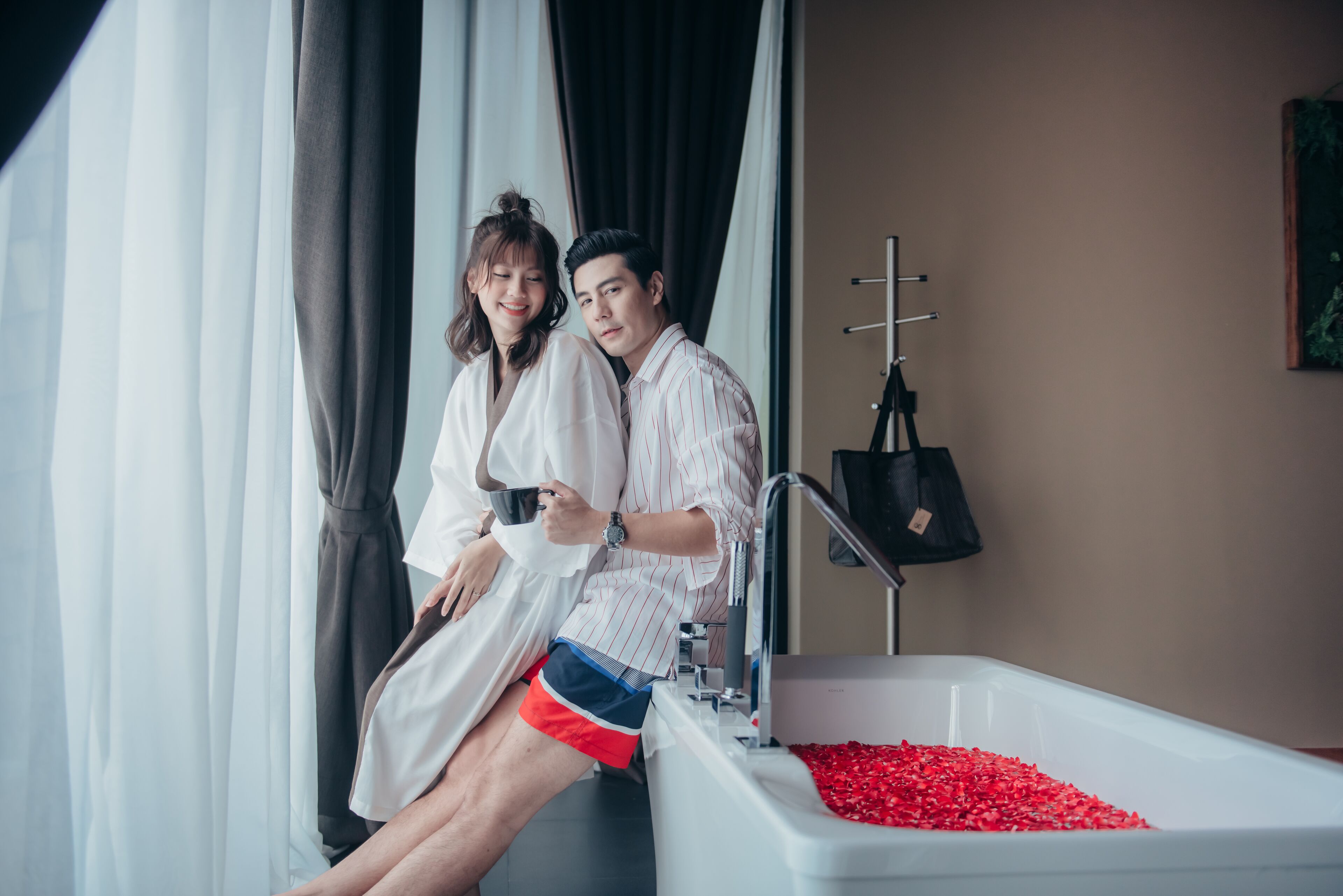 A couple sitting by a bathtub filled with red bath beads, with a towel rack and a painting on the wall.
