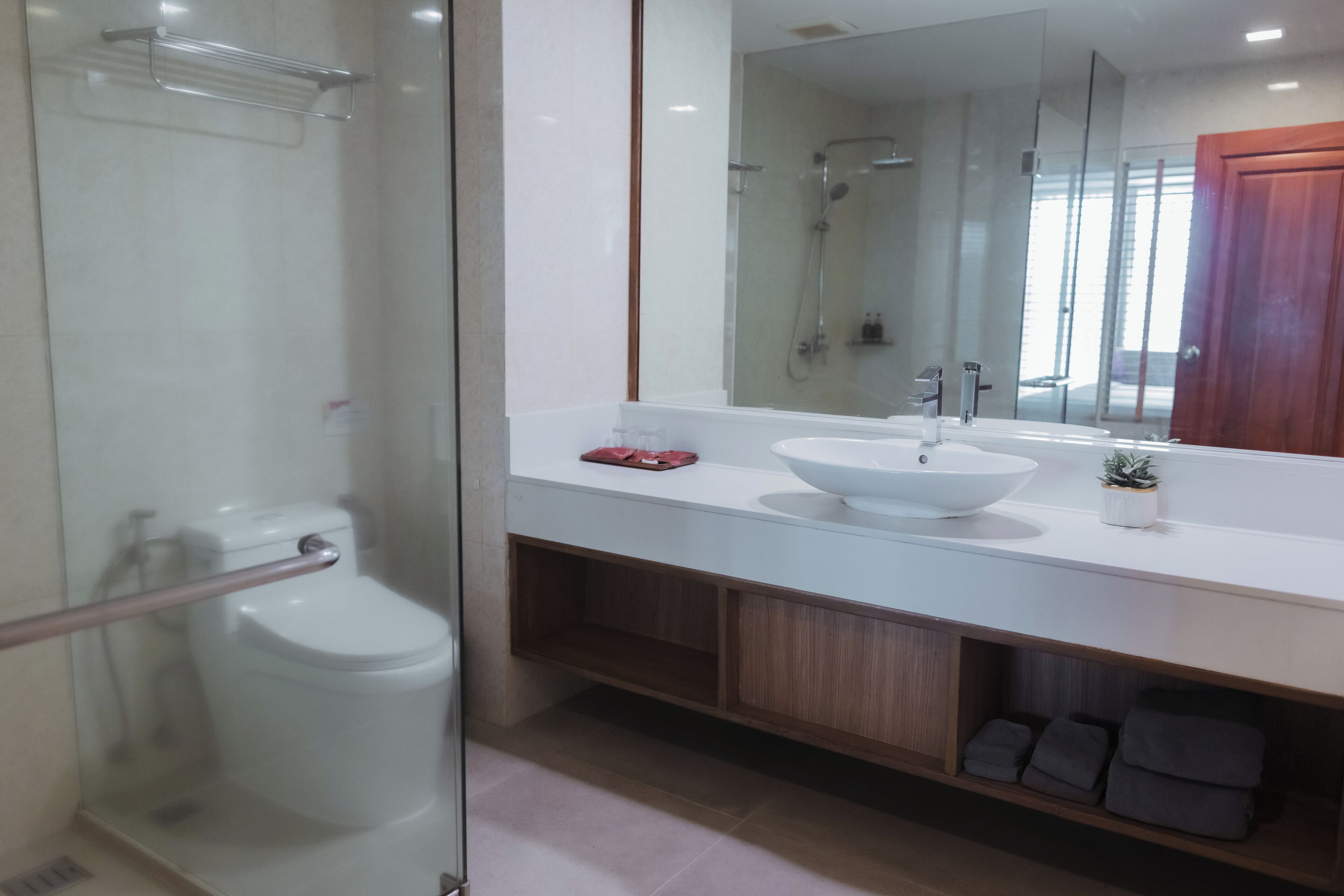 A modern bathroom with a glass shower enclosure, a white sink with a vessel basin, and a wooden vanity with storage.