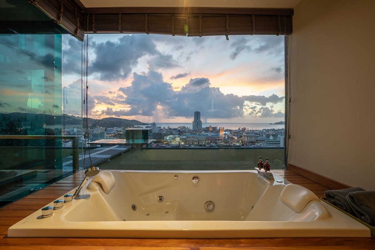 A modern bathroom with a large bathtub, a glass-enclosed shower area, and a city view.