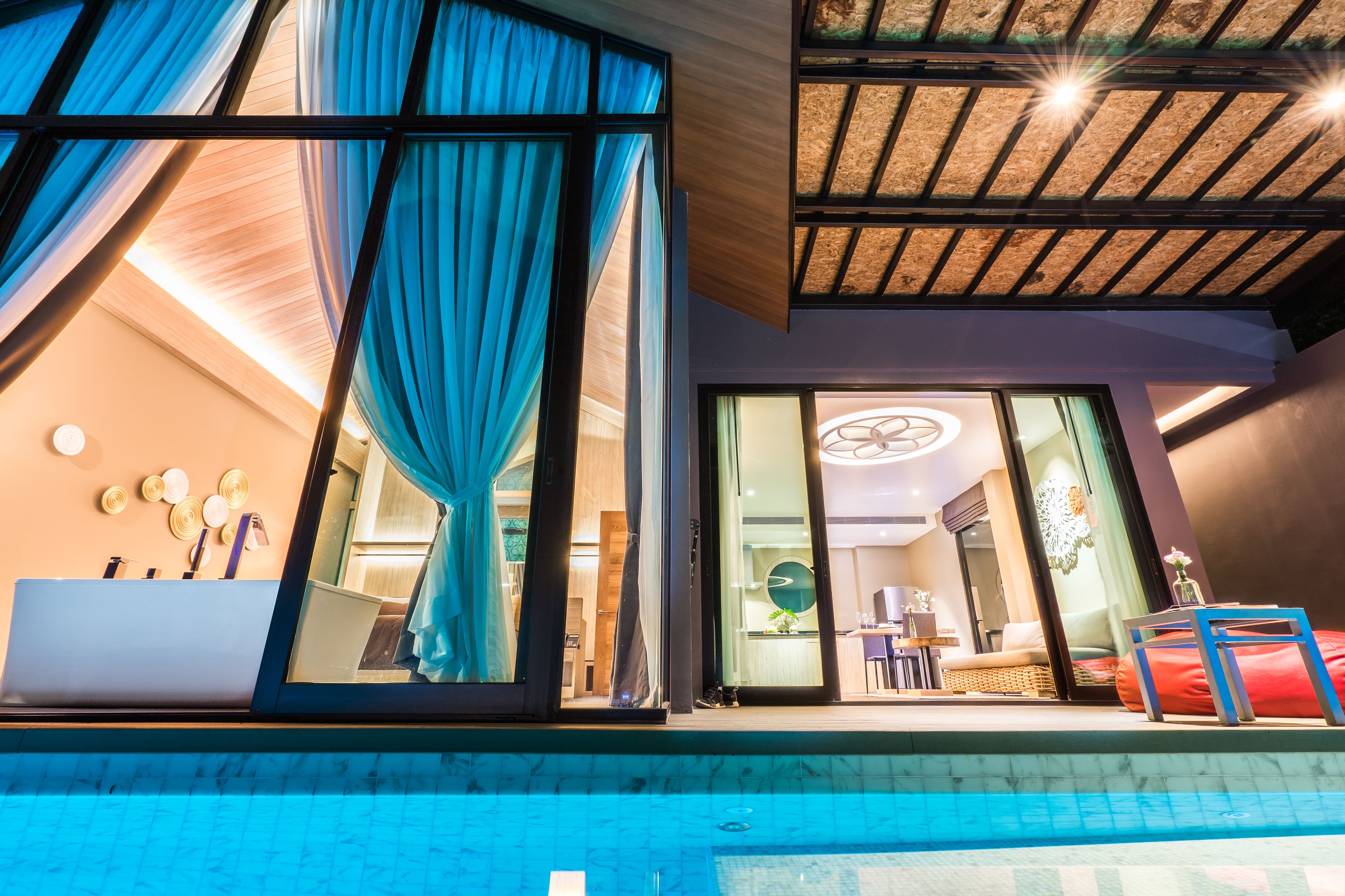 A modern hotel room with a large glass door, a pool, and a well-lit interior.
