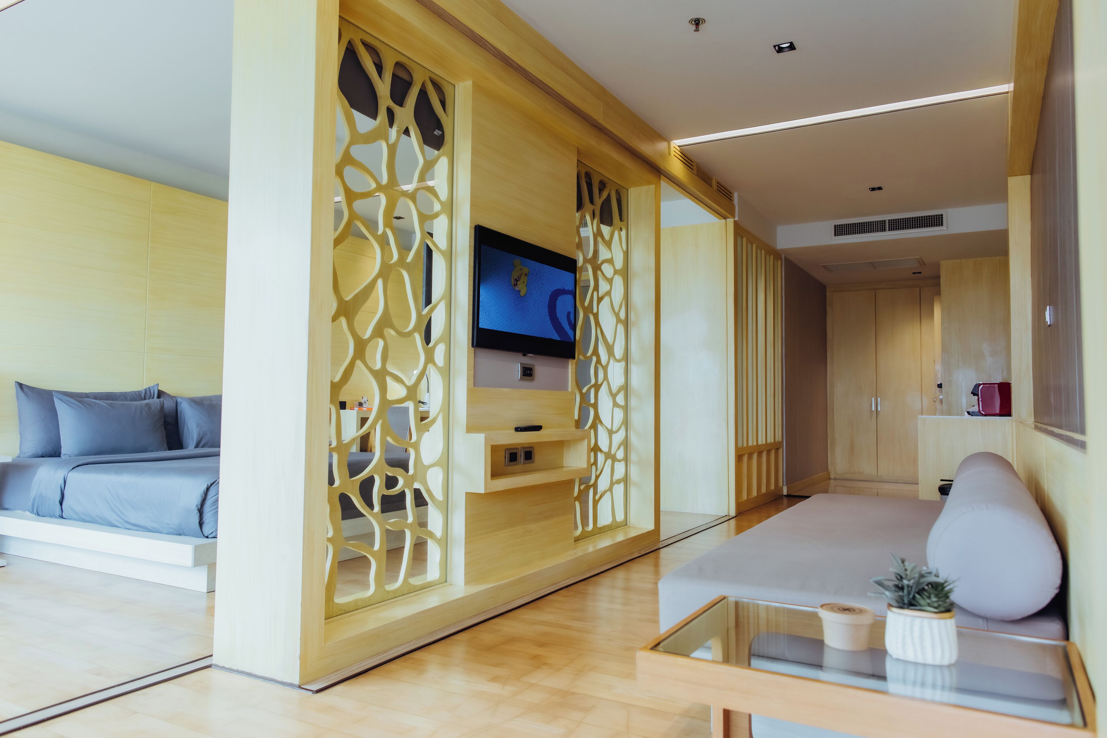 A modern hotel room with a bed, a TV, a sofa, and a decorative wooden screen.
