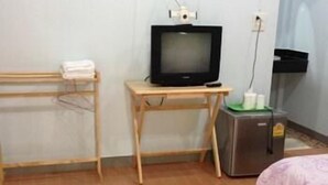 A hotel room with a wooden desk, a television, a bed with a floral bedspread, and a trash bin. - Baan Tai Rom Yen Resort (Surat Thani)