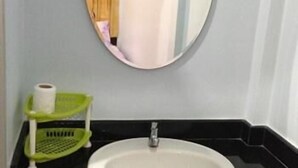 A bathroom with a round mirror, a white sink, and a green towel rack. - Baan Tai Rom Yen Resort (Surat Thani)