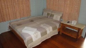 A bedroom with a bed, wooden nightstand, and curtains. - Baan Tai Rom Yen Resort (Surat Thani)