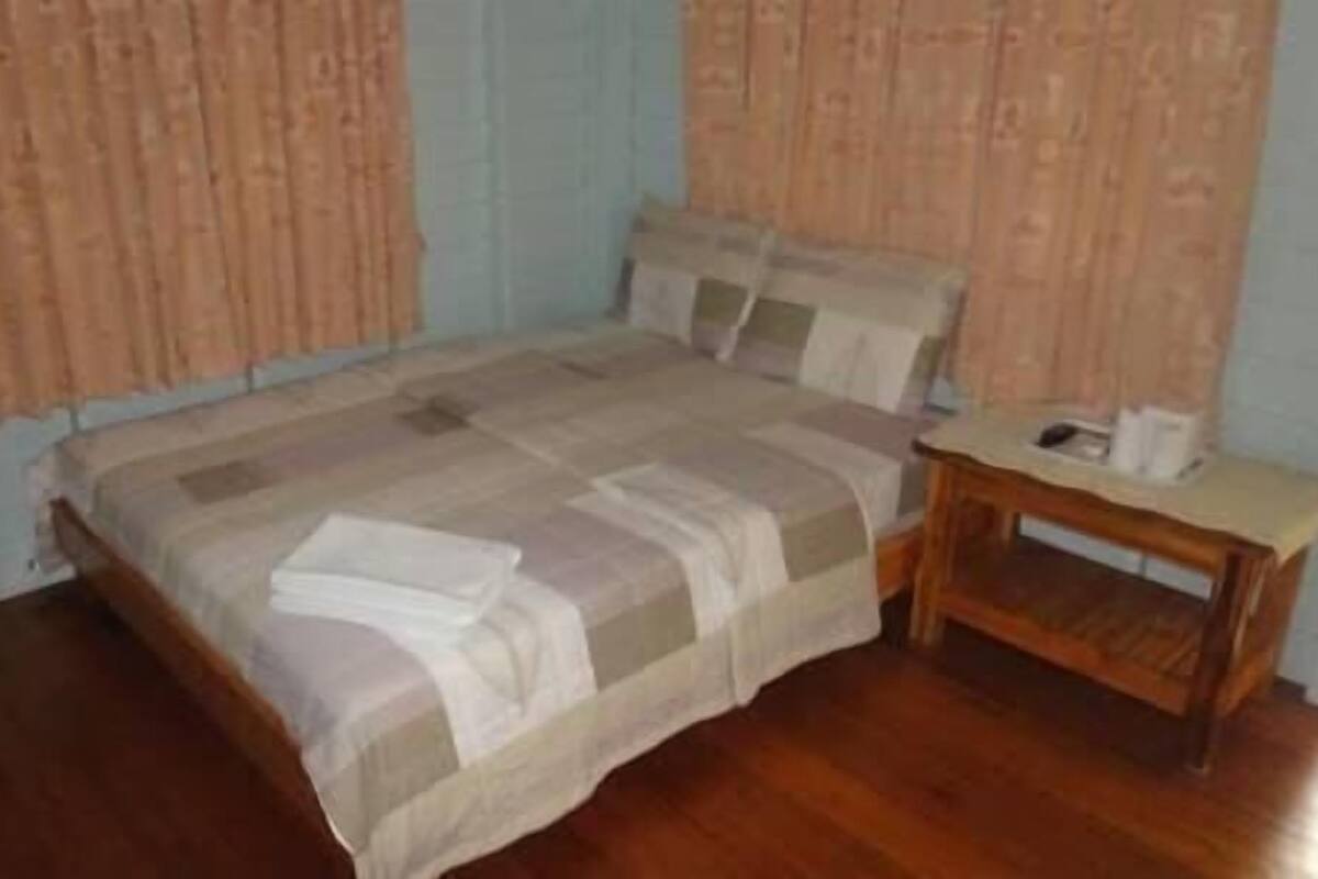 A bedroom with a bed, wooden nightstand, and curtains.
