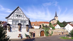 A traditional half-timbered building with a sign for Hotel Meisnerhof, a church with a spire, and a stone wall with flowers.