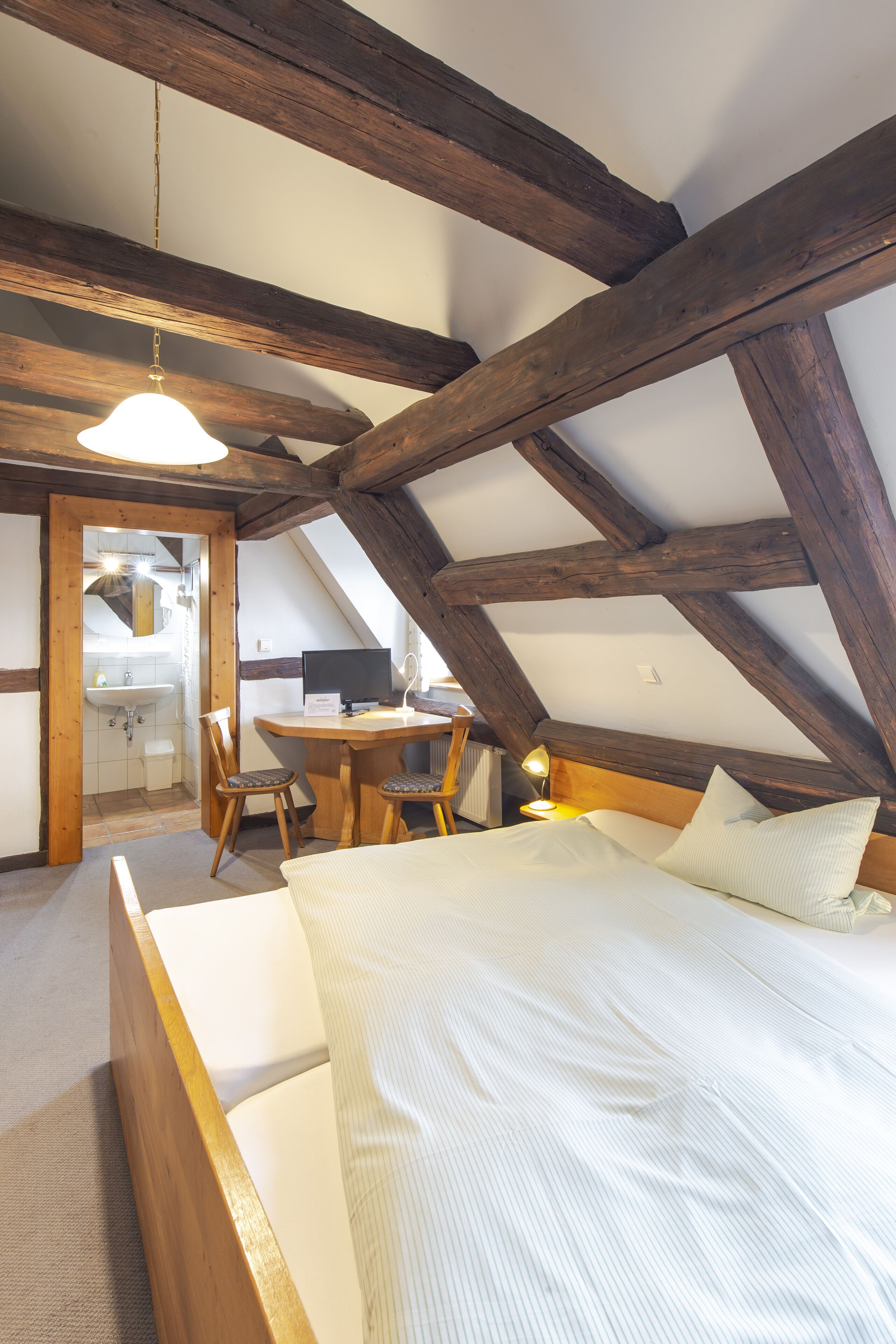 Un dormitorio con techo de madera, una cama, un escritorio y una silla.