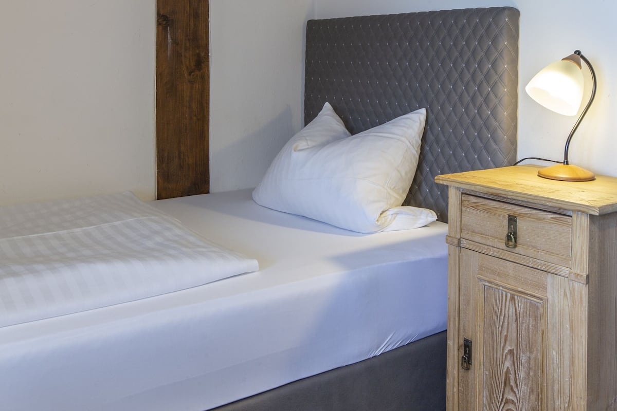 A neatly made bed with a wooden headboard, a bedside table with a lamp, and a small wooden cabinet.