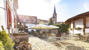 A cobblestone courtyard with outdoor seating, a church spire in the background, and a hotel sign. - Hotel Meisnerhof (Erlabrunn)