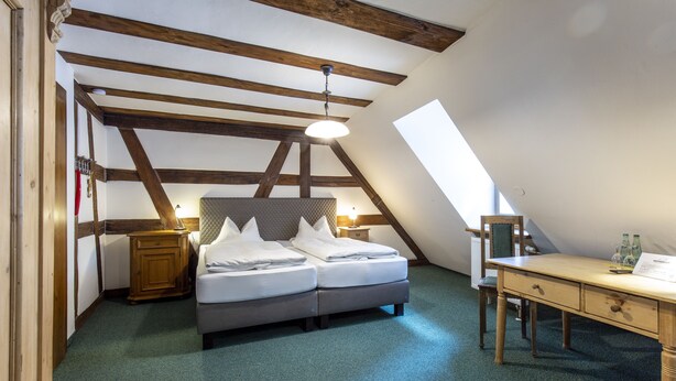 A bedroom with a loft-style ceiling, a bed, a desk, and a nightstand. - Hotel Meisnerhof (Erlabrunn)