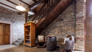 A rustic interior with stone walls, wooden beams, a wooden staircase, a wooden bookcase, and barrels.