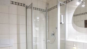 A bathroom with a glass-enclosed shower, a white sink, and a wooden bench.