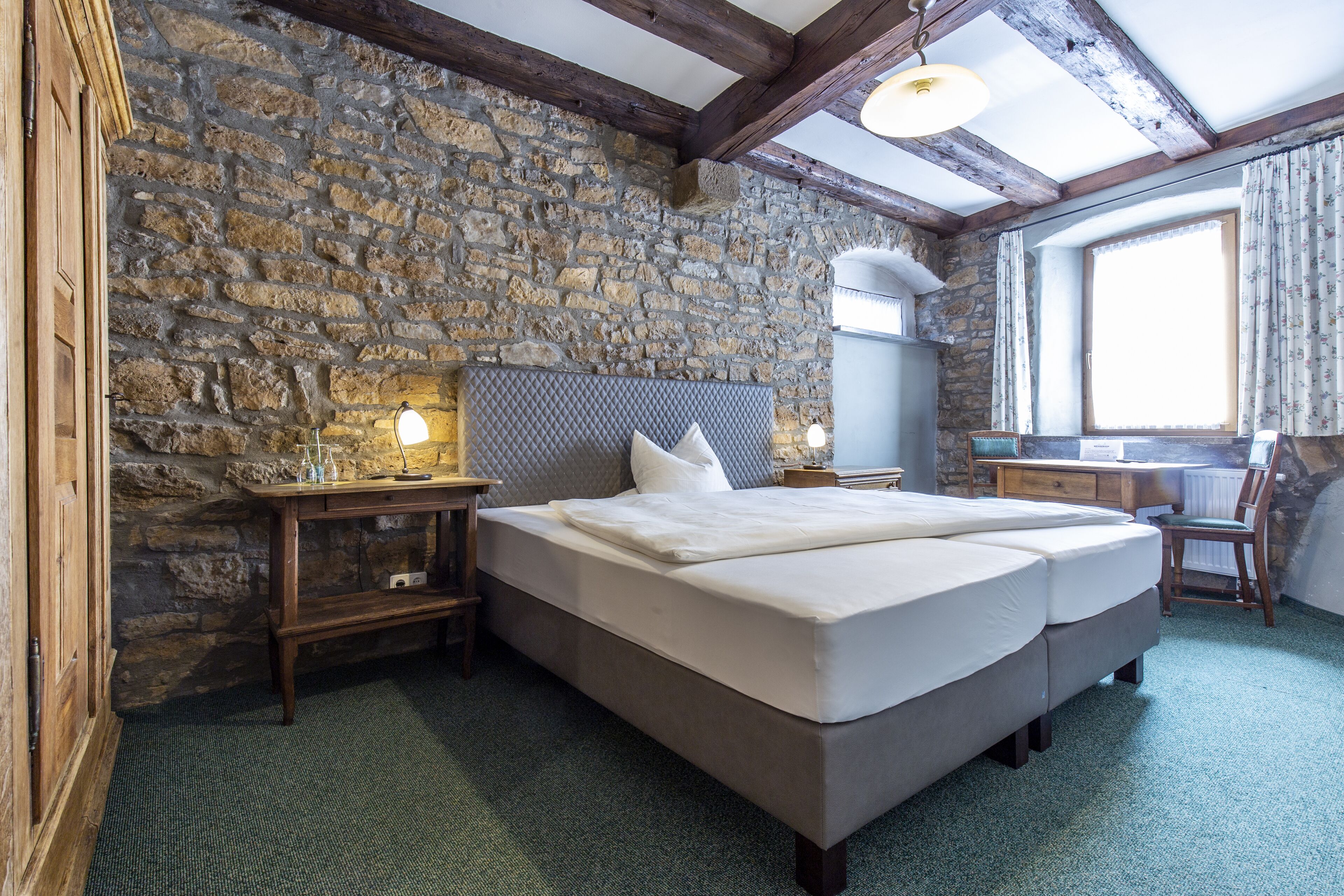 Ein Schlafzimmer mit Steinwand, einem Holzbett, einem Schreibtisch und einem Stuhl.