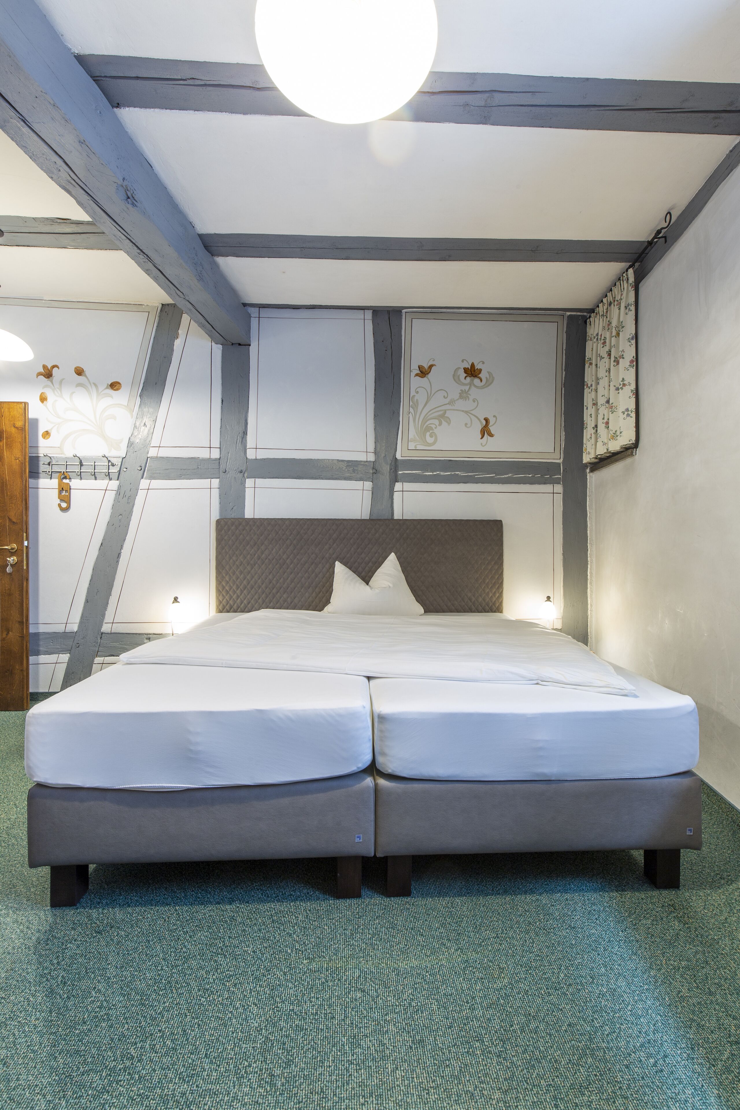 A double bed with a headboard, a green carpet, and a ceiling with exposed beams.