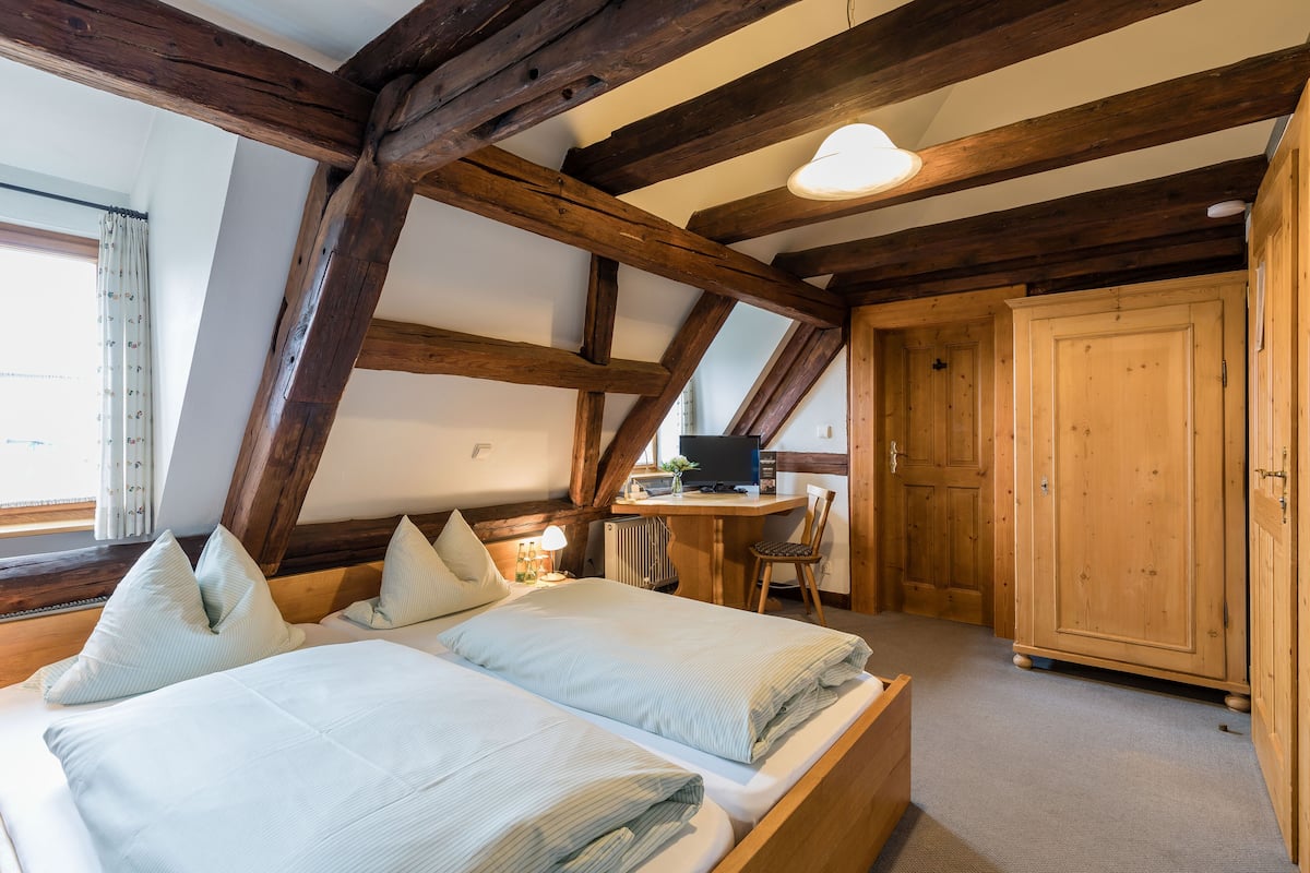 A bedroom with a wooden ceiling, a bed with pillows, a desk with a computer, and a wardrobe.