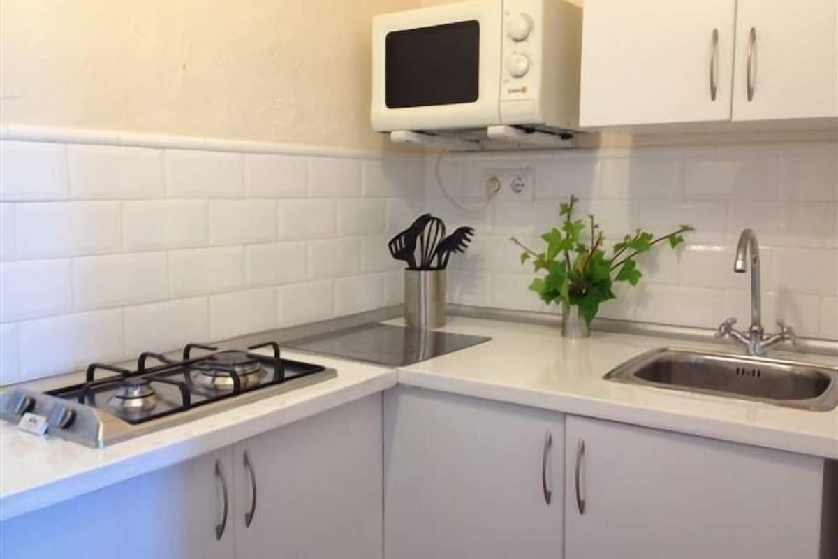 A compact kitchen with white cabinets, a gas stove, a microwave, and a sink.