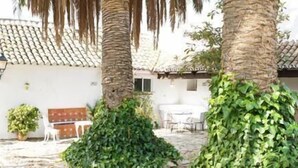 Un bâtiment doté d’un toit en tuiles, de murs blancs et d’une cour intérieure agrémentée de palmiers et de plantes en pot.