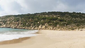 Une plage avec une colline rocheuse en arrière-plan.