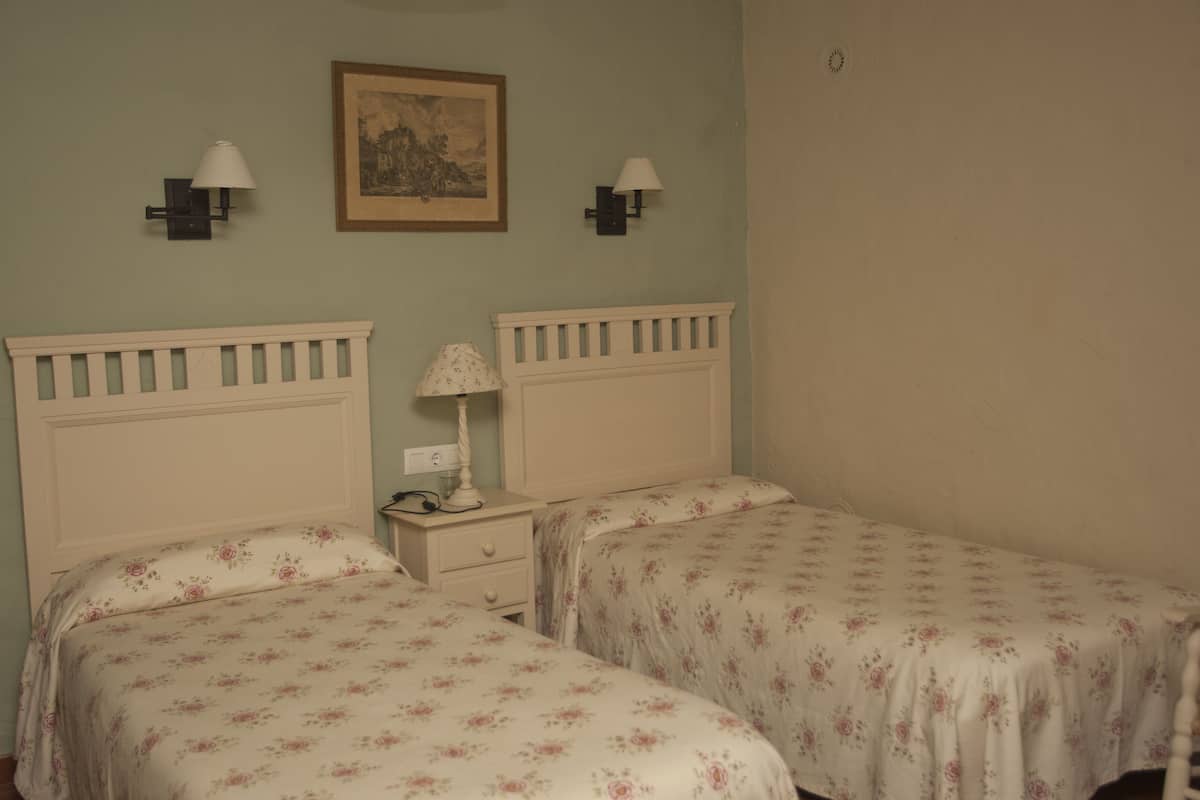 A room with two beds, each with a floral bedspread, a nightstand with a lamp, and two wall-mounted lamps.